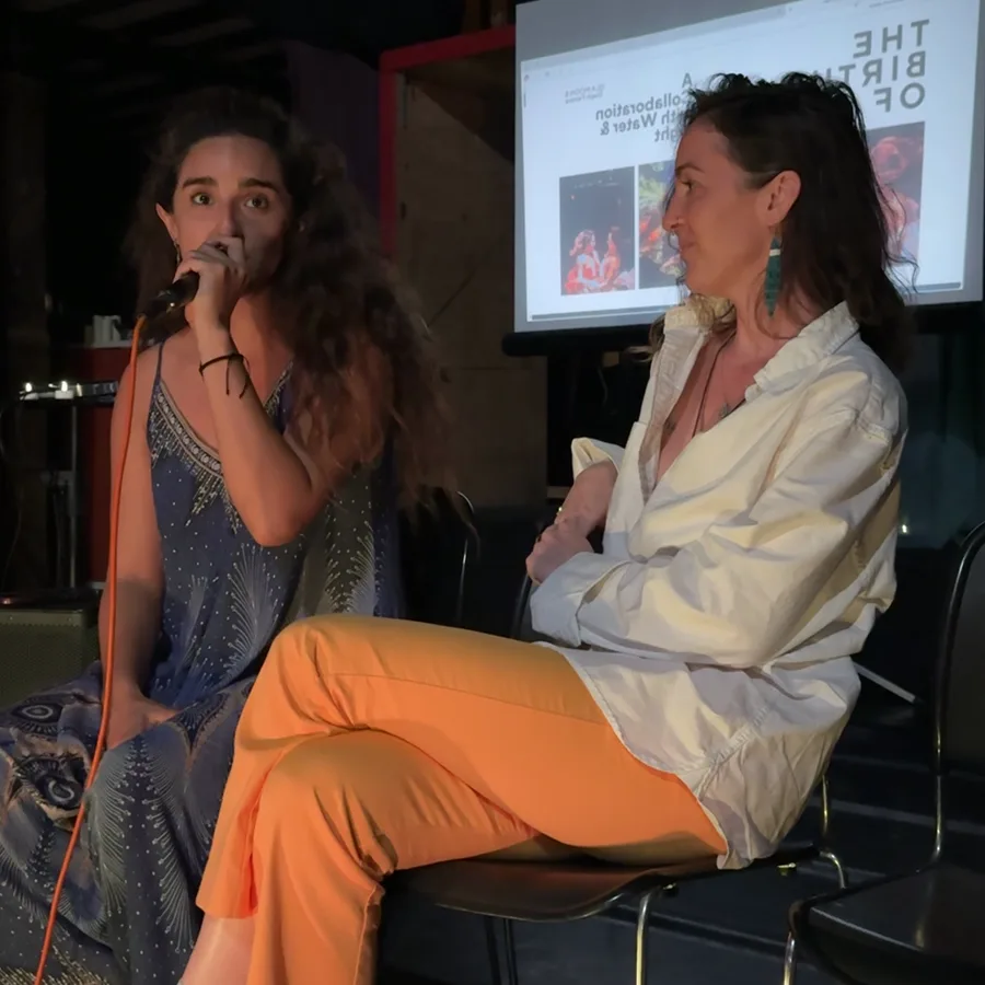 Steph Ferrera on stage in Austin, microphone in hand, in conversation beside a seated speaker.